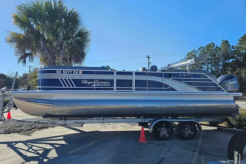 Slide: The Image of 2022 Bennington 24 LXFB pontoon boat on trailer, parked outdoors under clear sky. - 1