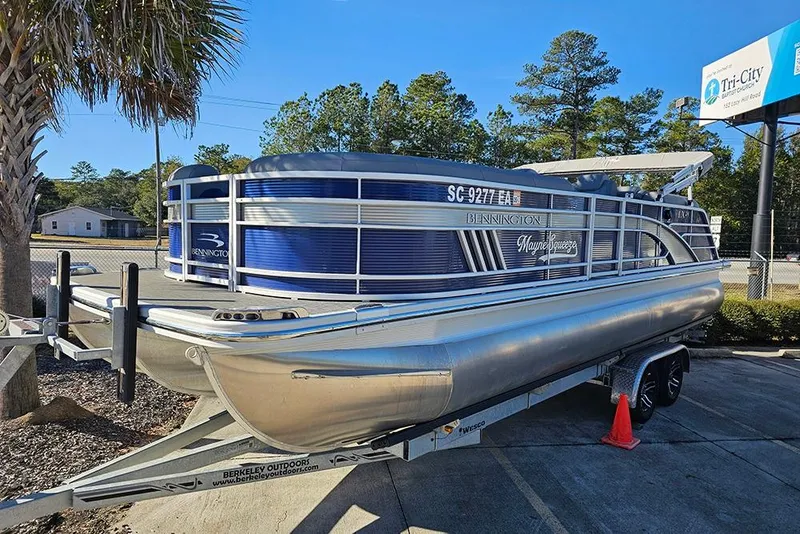 Slide: The Image of 2022 Bennington 24 LXFB pontoon boat on trailer, parked outdoors under clear blue sky. - 2