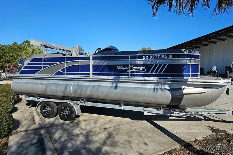 Slide: The Image of 2022 Bennington 24 LXFB pontoon boat on trailer, blue and silver design, parked outdoors. - 6