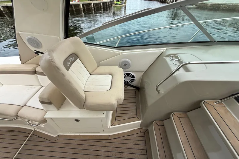 Slide: The Image of 2012 Sea Ray 370 Sundancer cockpit with beige seating and wooden flooring by the water. - 17