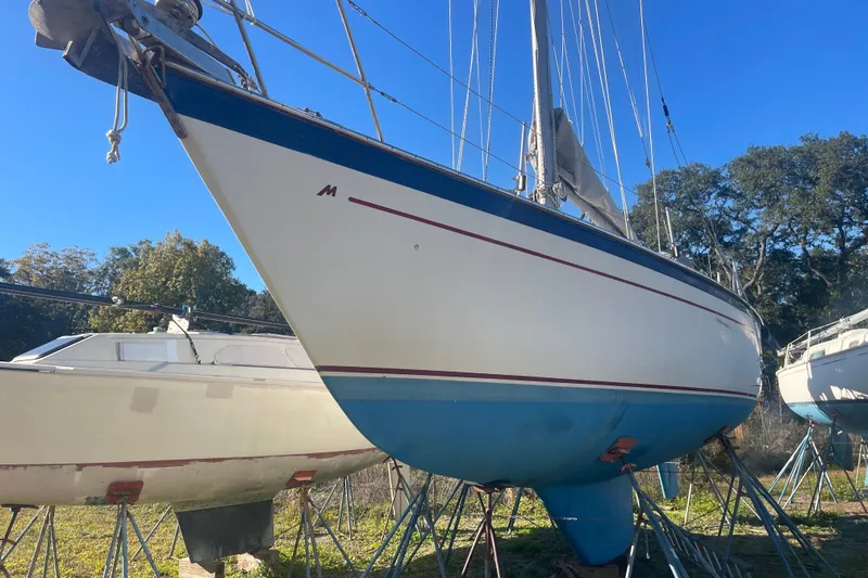 Slide: The Image of 1984 Morgan 384 sailboat on stands, blue and white hull, clear sky background. - 1