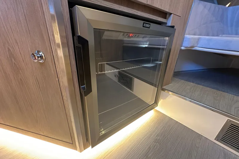 Slide: The Image of Mini fridge inside 2025 NX Boats 370, featuring sleek wood cabinetry and ambient lighting. - 51
