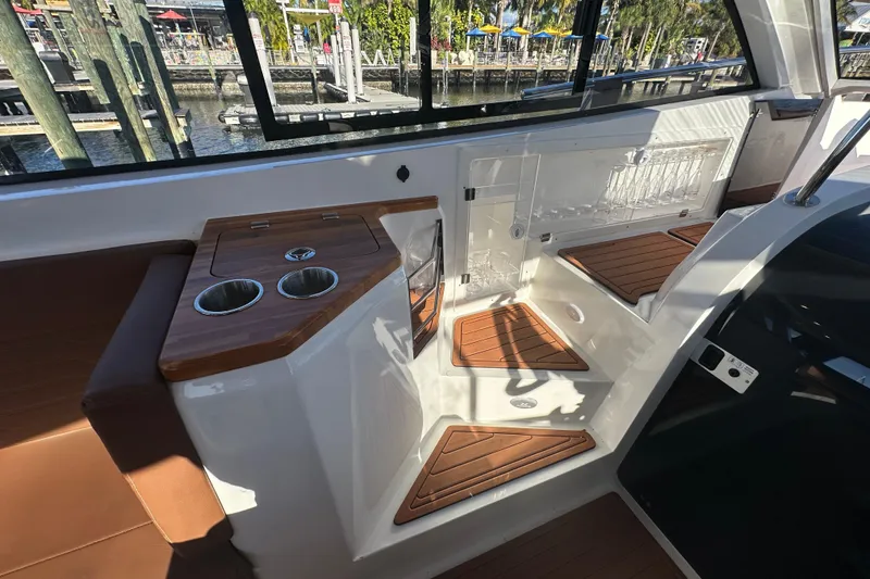 Slide: The Image of 2025 NX Boats 370 interior with wooden accents and cup holders, dockside view. - 80