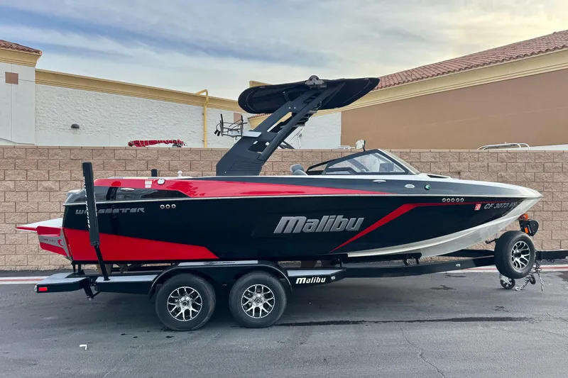 The Image of 2020 Malibu Wakesetter 22 LSV boat on trailer, black and red design, parked outdoors. - 0