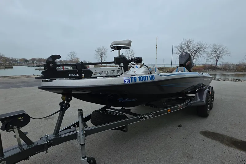 Slide: The Image of 2023 Bass Cat Caracal boat on trailer near a lake, overcast sky. - 2