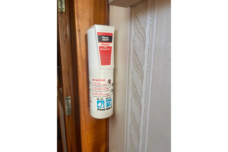 Slide: The Image of First Alert kitchen fire extinguisher mounted on a wooden wall inside a 1986 Mainship Mark III Motor Cruiser. - 53