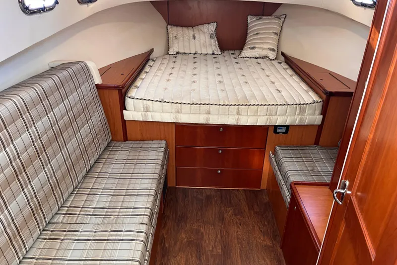 Slide: The Image of 2009 Mainship Pilot 31 cabin interior with bed, plaid seating, and wooden cabinetry. - 22