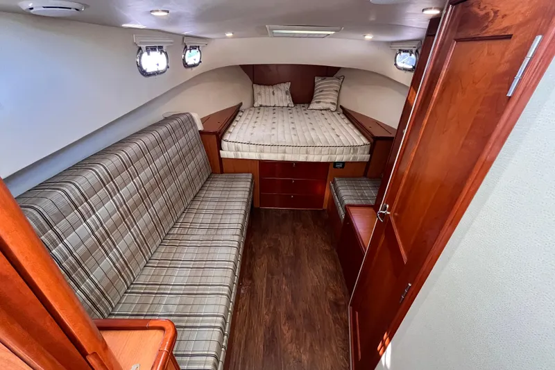 Slide: The Image of 2009 Mainship Pilot 31 cabin interior with bed, plaid sofa, and wooden furnishings. - 23