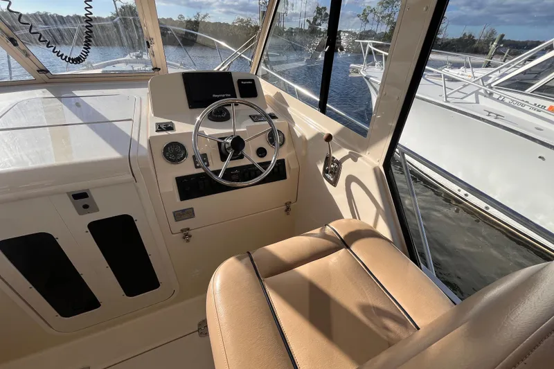 Slide: The Image of 2009 Mainship Pilot 31 helm with steering wheel, controls, and beige seating, docked by water. - 39