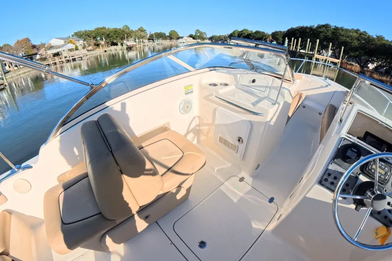 Slide: The Image of 2017 Scout 210 Dorado boat interior with beige seating and steering wheel, docked by a serene waterfront. - 19