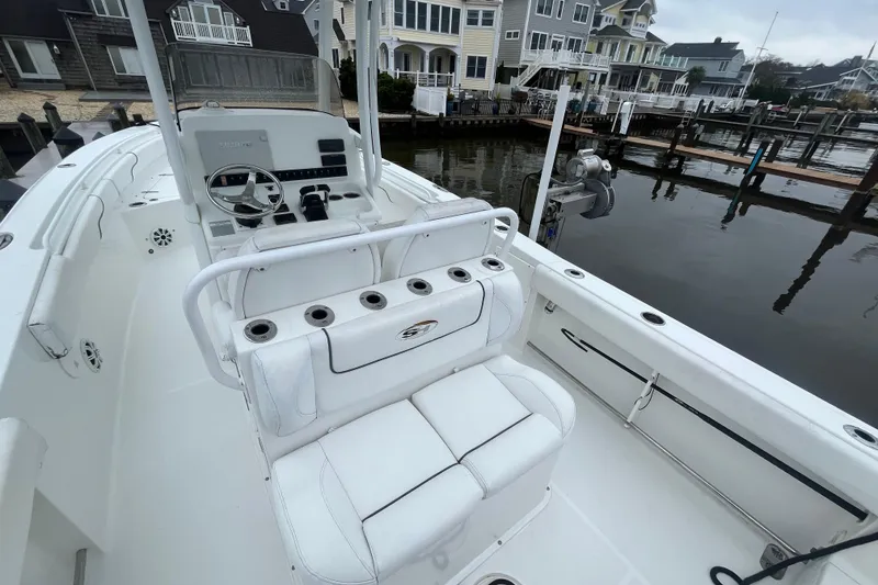 Slide: The Image of 2015 Sea Hunt Gamefish 27 boat interior with white seating and steering console, docked by waterfront homes. - 7