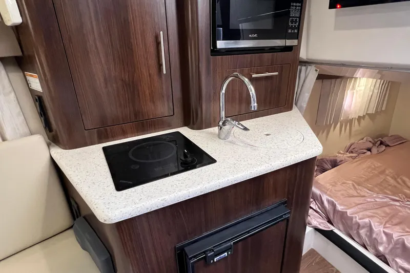 Slide: The Image of 2018 Regal 28 Express boat interior with kitchenette, featuring stove, sink, and microwave. - 35