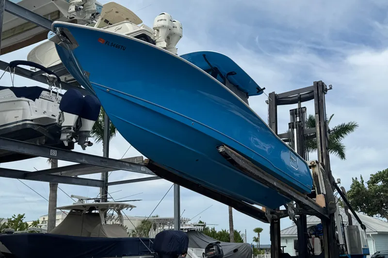 Slide: The Image of 2024 Sea Hunt Ultra 305 SE boat in vibrant blue, elevated on a forklift at a marina. - 19