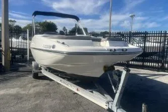 Slide: The Image of 2018 Bayliner 210 Deck Boat on trailer, parked outdoors under blue sky. - 2