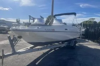 Slide: The Image of 2018 Bayliner 210 Deck Boat on trailer, parked outdoors under clear blue sky. - 3