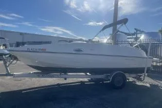 Slide: The Image of 2018 Bayliner 210 Deck Boat on trailer under clear blue sky. - 4