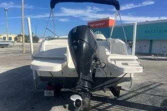 Slide: The Image of 2018 Bayliner 210 Deck Boat with outboard motor, parked outdoors. - 5