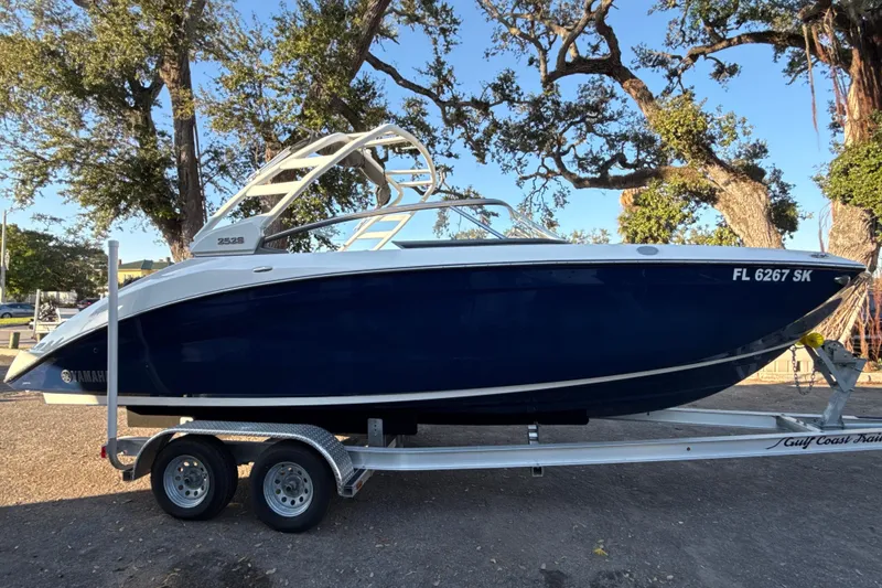 The Image of 2021 Yamaha Boats 252S on trailer, parked outdoors with trees in the background. - 0