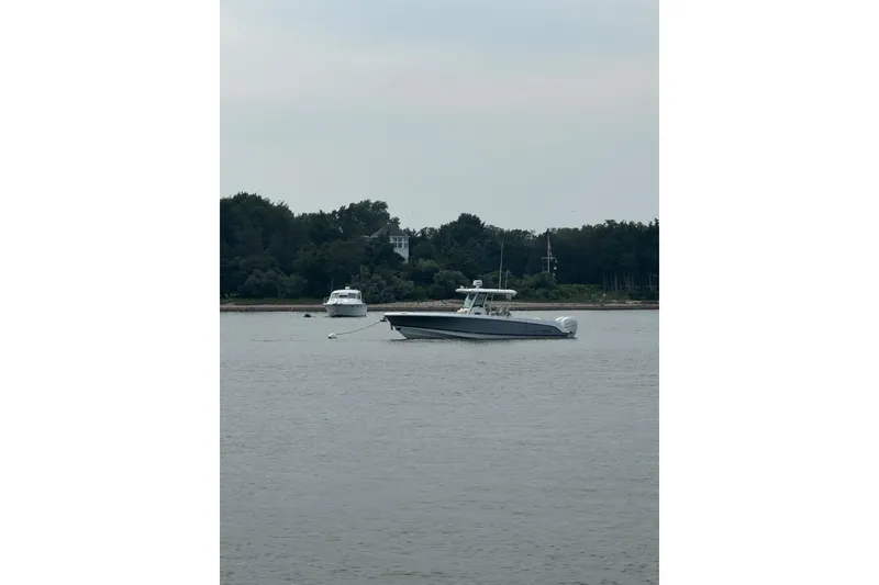 Slide: The Image of 2018 Boston Whaler 330 Outrage boat on calm water near a wooded shoreline. - 1