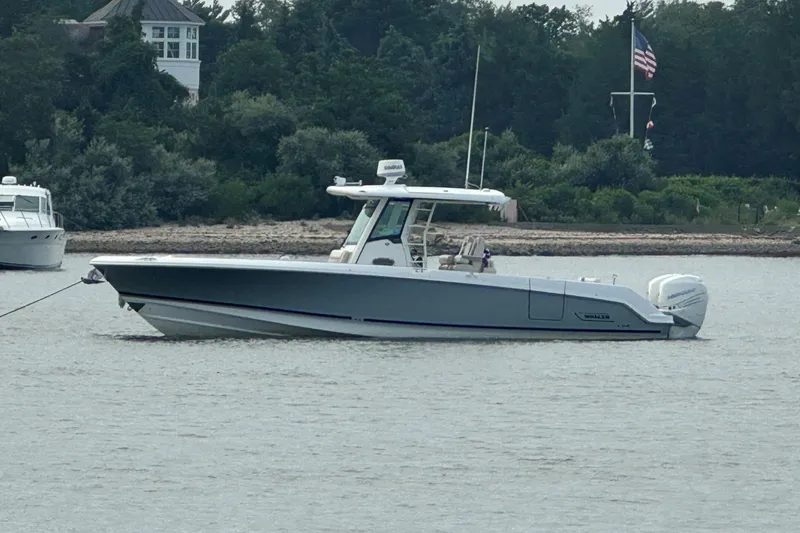 Slide: The Image of 2018 Boston Whaler 330 Outrage boat anchored on calm water near a wooded shoreline. - 2