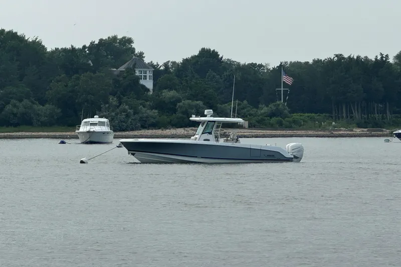 Slide: The Image of 2018 Boston Whaler 330 Outrage boat anchored on calm water near a wooded shoreline. - 3