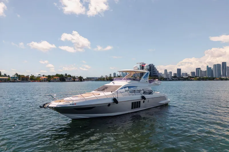Slide: The Image of 2016 Azimut 64 Flybridge yacht on calm water with city skyline in background. - 2