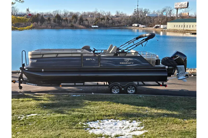The Image of 2024 Regency 250 LE3 Sport pontoon boat on trailer by a serene lake. - 0