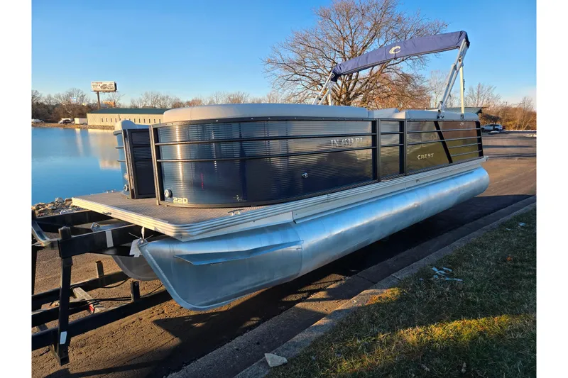 Slide: The Image of 2022 Crest Classic LX 220 pontoon boat on trailer by a lake. - 7