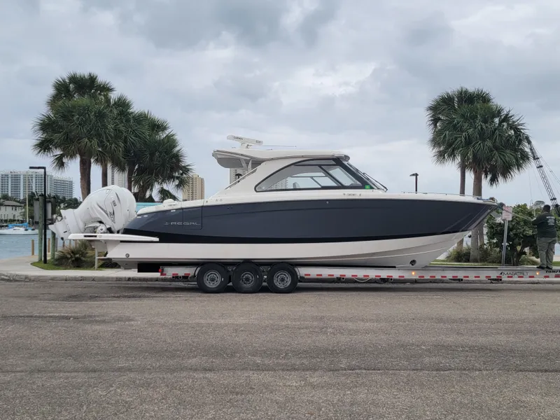 Slide: The Image of 2022 Regal LX36 boat on trailer, parked near palm trees under cloudy sky. - 6