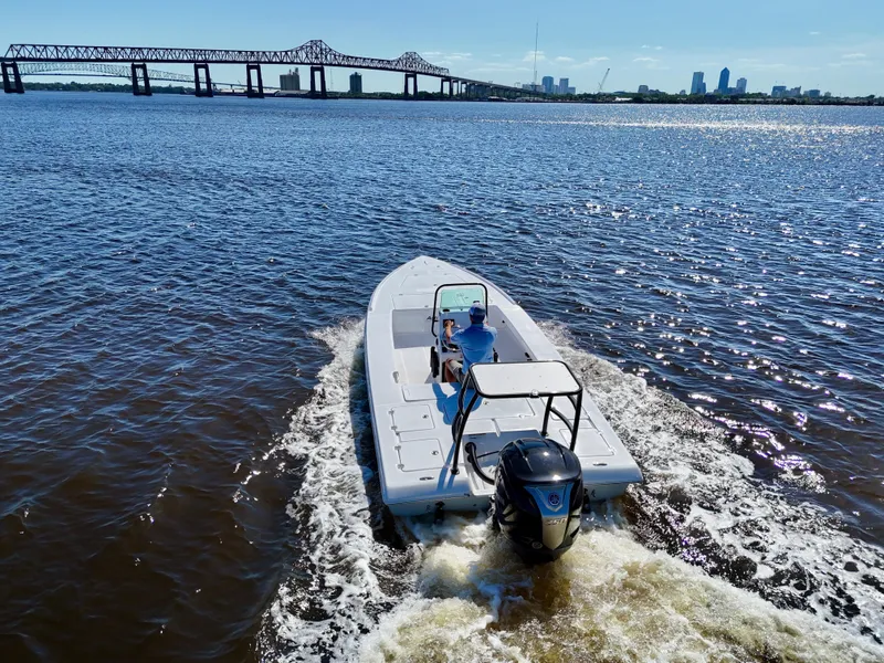 Slide: The Image of 2025 Action Craft 20 Flats boat cruising on a river near a city skyline and bridge. - 7