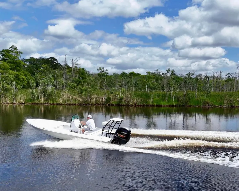 Slide: The Image of 2025 Action Craft 17 Flats boat cruising on a scenic river under a cloudy sky. - 19