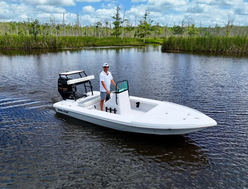 Slide: The Image of 2025 Action Craft 17 Flats boat on calm water with lush greenery background. - 4