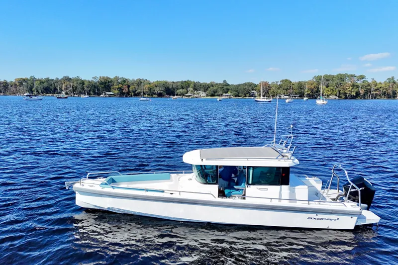Slide: The Image of 2020 Axopar 28 CABIN boat on a serene lake with forested shoreline. - 18