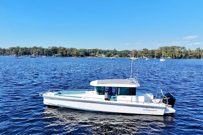 Slide: The Image of 2020 Axopar 28 CABIN boat cruising on a serene lake with forested shoreline. - 19