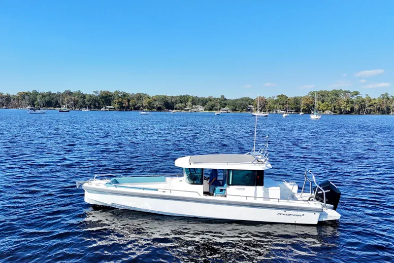 Slide: The Image of 2020 Axopar 28 CABIN boat cruising on a serene lake with forested shoreline. - 20