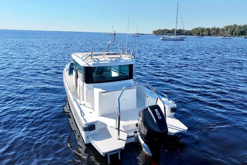 Slide: The Image of 2020 Axopar 28 CABIN boat on calm blue water with distant sailboats. - 24