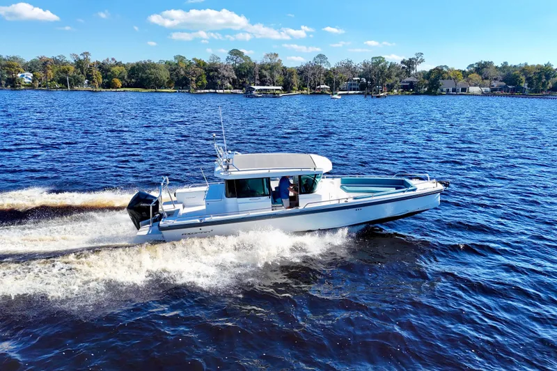 Slide: The Image of 2020 Axopar 28 CABIN cruising on a sunny lake with scenic shoreline. - 32