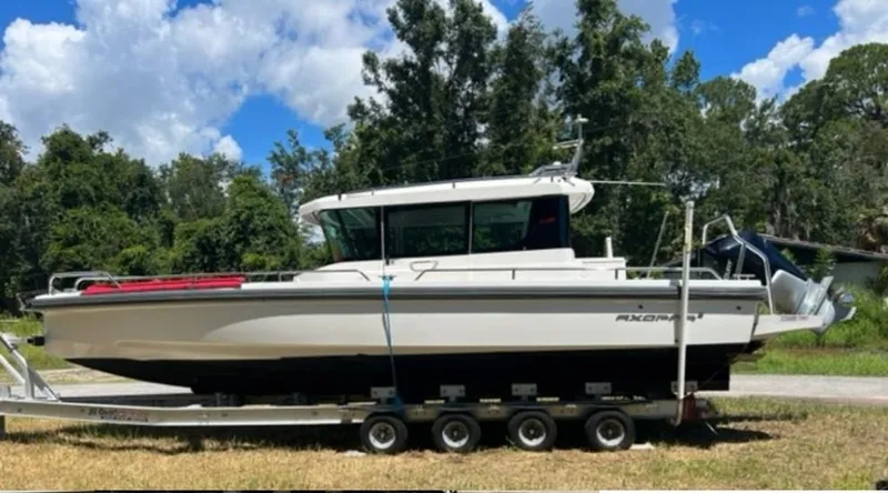 Slide: The Image of 2020 Axopar 28 boat on trailer, surrounded by trees and blue sky. - 59