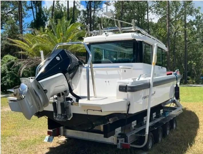 Slide: The Image of 2020 Axopar 28 boat on trailer, parked outdoors with trees in the background. - 60