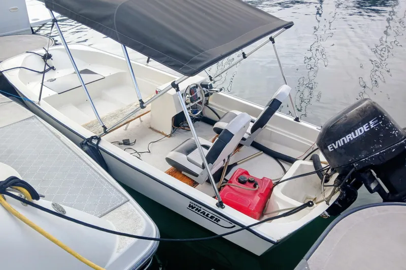 Slide: The Image of A small motorboat with canopy, Evinrude engine, and seating, docked beside a larger yacht. - 32