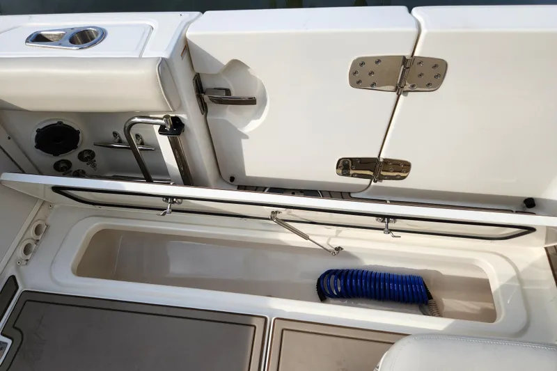 Slide: The Image of 2022 Boston Whaler 330 Outrage boat storage compartment with blue hose and stainless steel fixtures. - 47