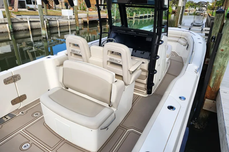 Slide: The Image of 2022 Boston Whaler 330 Outrage boat interior with seating and helm, docked by the water. - 8