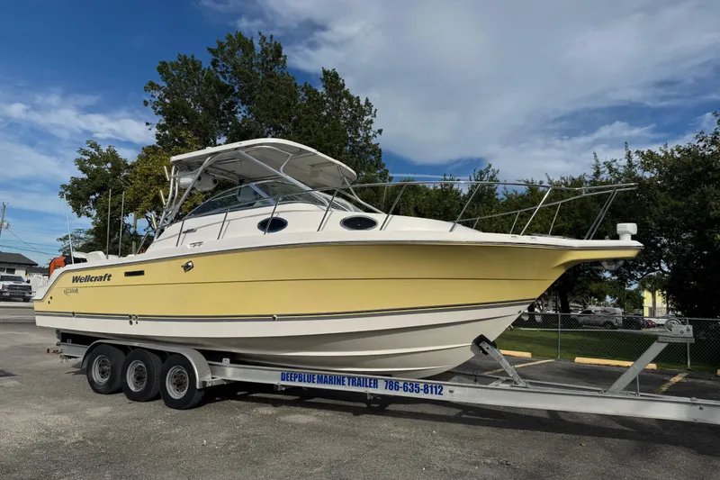 The Image of 2005 Wellcraft 290 Coastal boat on trailer, yellow hull, parked outdoors. - 0