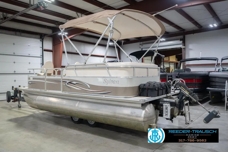 Slide: The Image of 2009 Sylvan 818 Mirage Fish pontoon boat in indoor storage, featuring a canopy and trailer. - 10