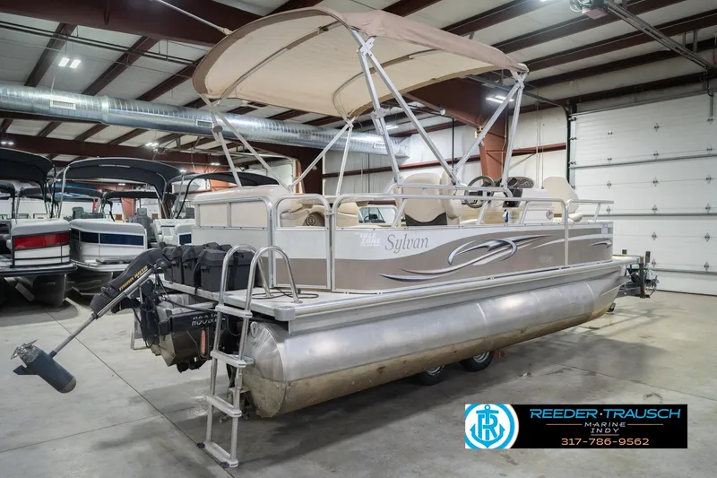 Slide: The Image of 2009 Sylvan 818 Mirage Fish pontoon boat in indoor showroom, featuring canopy and motor. - 8