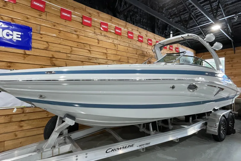 The Image of 2026 Crownline 298 SS boat on trailer in showroom, wooden wall background. - 1