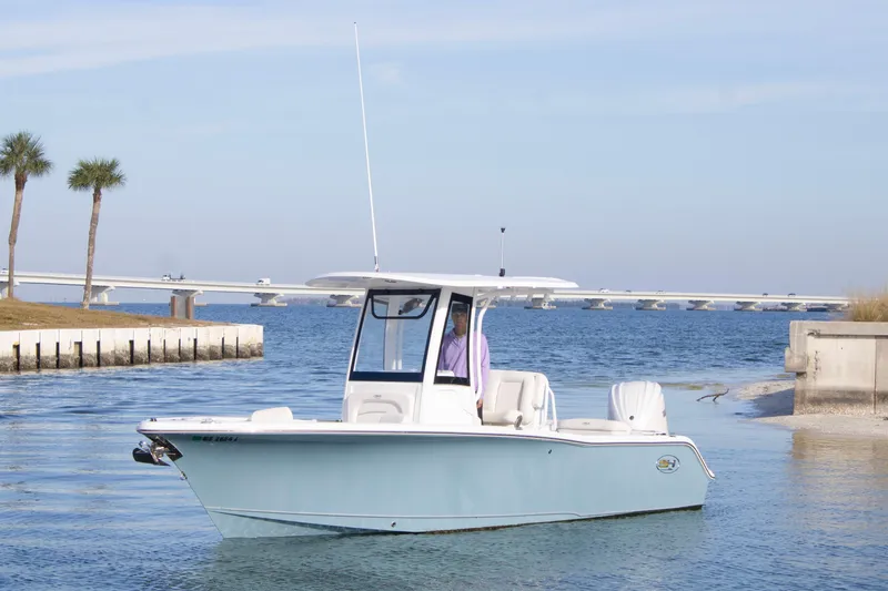 Slide: The Image of 2026 Sea Hunt Ultra 245 SE boat on calm water near a bridge and palm trees. - 2