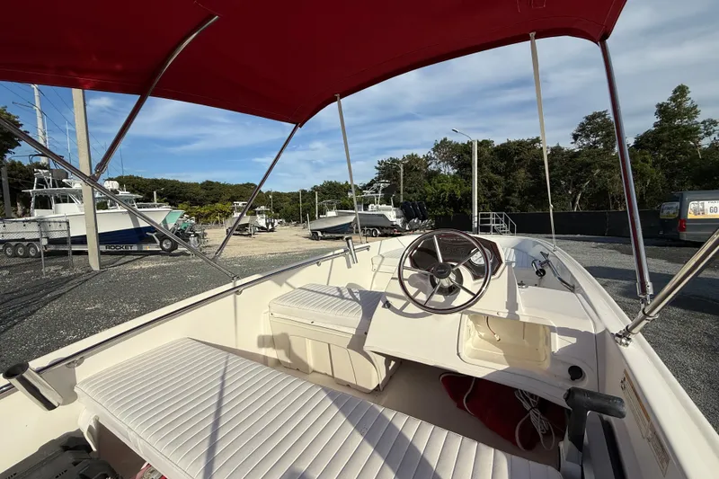 Slide: The Image of 2017 Boston Whaler 150 Super Sport boat interior with red canopy and steering wheel. - 7