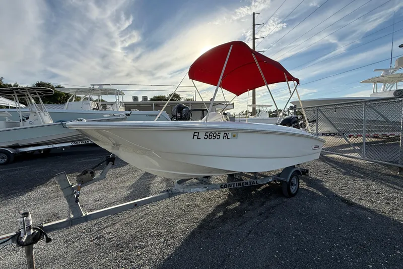Slide: The Image of 2017 Boston Whaler 150 Super Sport boat with red canopy on trailer, parked outdoors. - 8