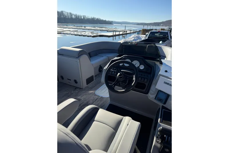 Slide: The Image of 2026 Bentley Pontoons Legacy 243 Navigator interior with steering wheel and seating, docked by a snowy lake. - 7